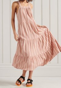 Abito maxi a righe in rosso e crema, con spalline sottili, design a strati e una gonna fluente. Abbinato a sandali neri con suole arancioni.