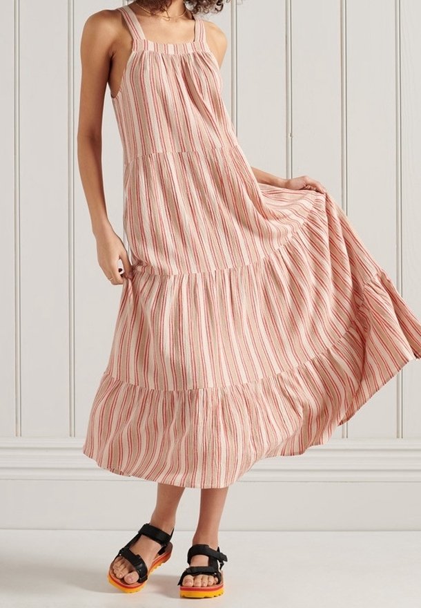 Abito maxi a righe in rosso e crema, con spalline sottili, design a strati e una gonna fluente. Abbinato a sandali neri con suole arancioni.