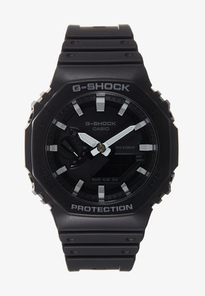 Reloj G-Shock negro con esfera redonda, display digital y analógico, acentos grises y correa de goma texturizada. Resistente al agua hasta 20 bares.