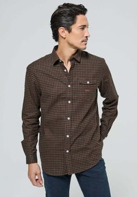 Chemise à carreaux marron et orange à manches longues, avec un col boutonné à l'avant et une poche poitrine unique. Fabriquée à partir d'un tissu à texture douce.