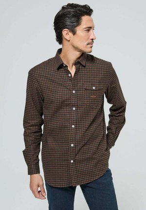 Chemise à carreaux marron et orange à manches longues, avec un col boutonné à l'avant et une poche poitrine unique. Fabriquée à partir d'un tissu à texture douce.