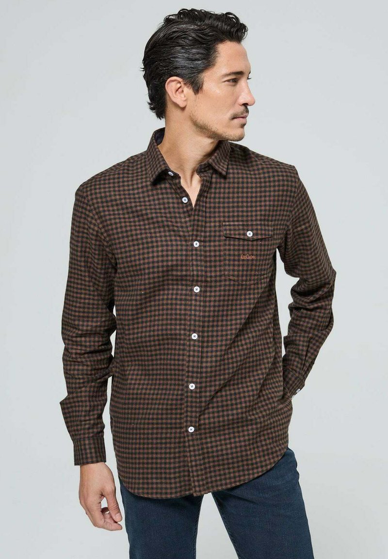 Chemise à carreaux marron et orange à manches longues, avec un col boutonné à l'avant et une poche poitrine unique. Fabriquée à partir d'un tissu à texture douce.