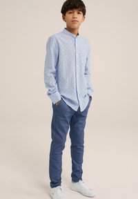 Lichtblauw overhemd met kleine zwarte stippen, gecombineerd met donkerblauwe slim-fit broek en witte sneakers. Gladde stof en moderne pasvorm.
