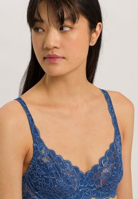 Svetle modrý krajkový bralet s intricate květinovými vzory, nastavitelnými krajkovými ramínky a měkkým, nevyztuženým designem s vlnitým dekoltem.