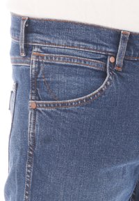 Donkerblauwe denim jeans met oranje stiksel, voorzien van een voorzak en rits. De stof heeft een soepele textuur en een klassieke pasvorm.