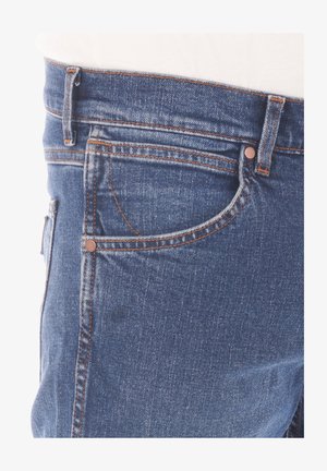 Granatowe dżinsy z pomarańczowymi przeszyciami, z przednią kieszenią i zamkiem błyskawicznym. Tkanina ma gładką teksturę i klasyczny fason.