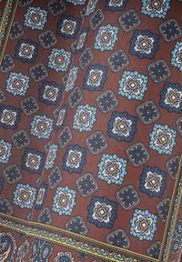 Brązowa tkanina z powtarzającym się wzorem kwiatowym w odcieniach niebieskiego, białego i granatowego, z akcentami żółtego w projekcie obramowania.