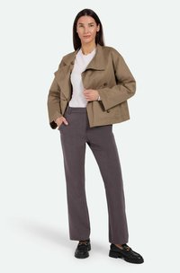 Chaqueta corte cropped en caqui con botones de doble fila, camisa blanca y pantalones grises de corte entallado. Los zapatos son mocasines negros con un acento dorado.