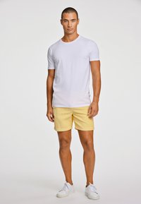 Vit T-shirt i slim fit kombinerad med gula kordbyxor, som visar en texturerad yta, kompletterad med vita sneakers.