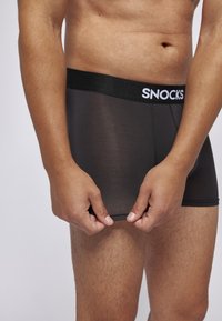 Schwarze, enganliegende Boxershorts mit einem elastischen Bund mit Logo. Der Stoff ist glatt und halbtransparent und präsentiert ein enganliegendes Design.