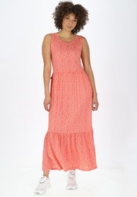 Korallenrobes Maxi-Kleid mit weißen Blumenmuster, ärmellos und mit Rüschensaum, kombiniert mit weißen Turnschuhen.
