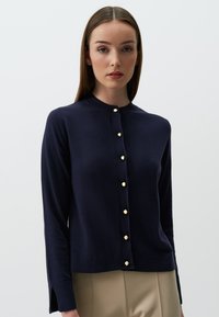 Navy-blaues Strickjacke aus weichem Material, mit rundem Halsauschnitt, langen Ärmeln und goldenen Knopfdetails an der Vorderseite.