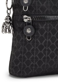 Black nylon bag featuring a geometric pattern, zippered pocket, and a decorative silver monkey keychain. Smooth texture and durable design.