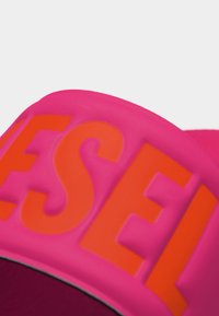 Rosa stoff med store oransje bokstaver som delvis staver "MESSEL" på en buet overflate, muligens en hatt eller veske.