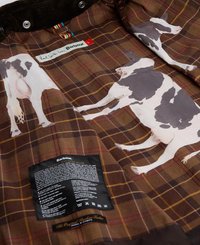 Forro de um casaco xadrez castanho com vacas impressas, collar canelado e etiqueta de cuidados anexada. O material parece texturizado e durável.