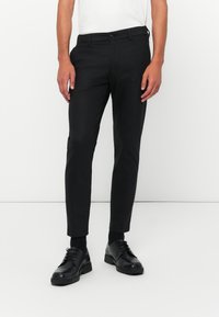 Zwarte broek met een slim fit ontwerp, gemaakt van soepel stof. Beschikt over een tailleband met riemlussen en zijzakken. Draagt men met zwarte schoenen.