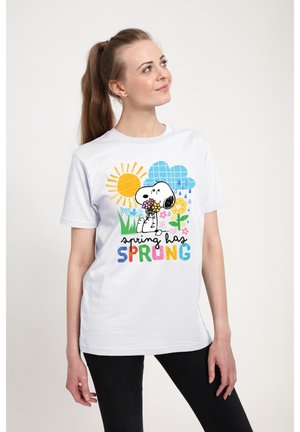 Ung kvinde iført hvid T-shirt med Snoopy, der holder blomster, sol, regndråber og teksten "foråret er startet" i farverige bogstaver.