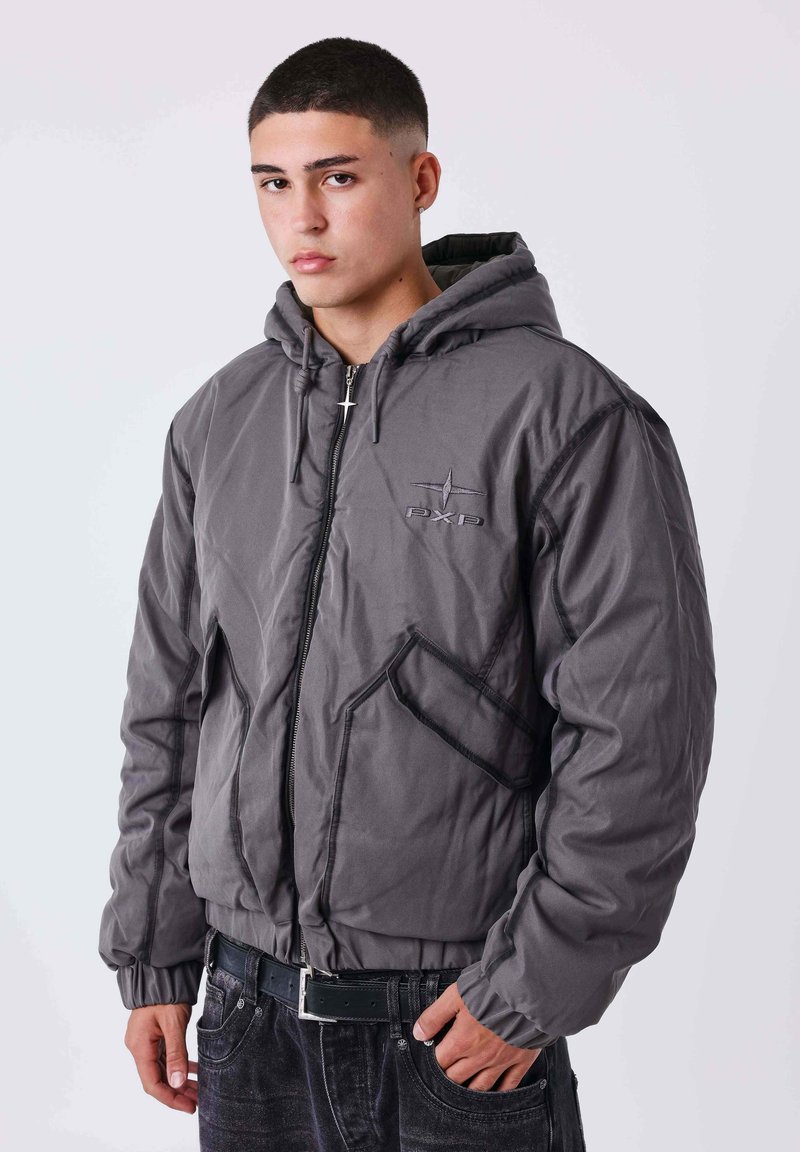 Veste à capuche grise avec fermeture éclair, poignets élastiques et deux poches avant. Présente un logo discret sur la poitrine et des coutures contrastantes.