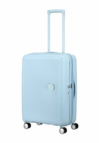 Valigia rigida di colore azzurro chiaro, con un design a texture ondulata, manico retrattile e quattro ruote piroettanti per una facile mobilità.