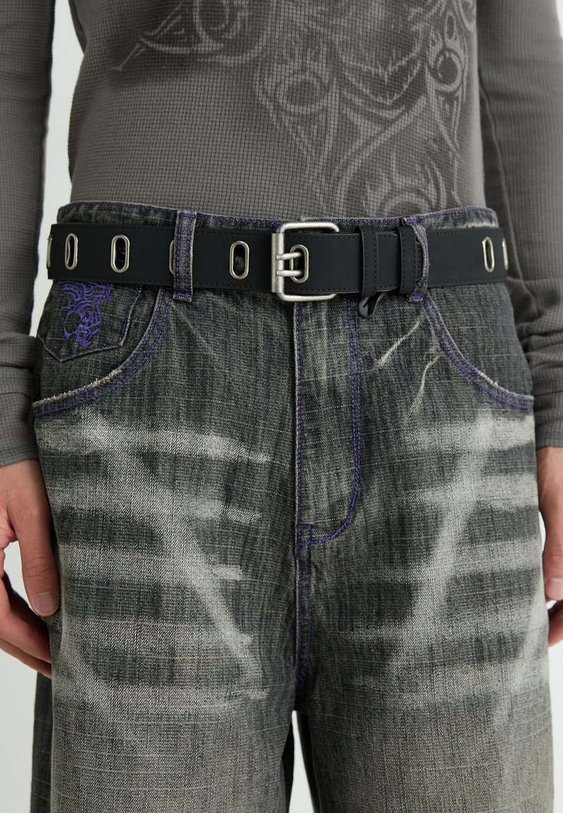 Donkerdenim jeans met vervaagde en versleten gebieden, geaccentueerd met paarse stiksels en een zwarte riem met een metalen oogjes.
