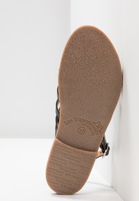 Sandalía negra con tiras y suela de goma texturizada, que presenta el nombre de la marca "Les Tropéziennes" y el tamaño 37 grabado en la parte inferior.