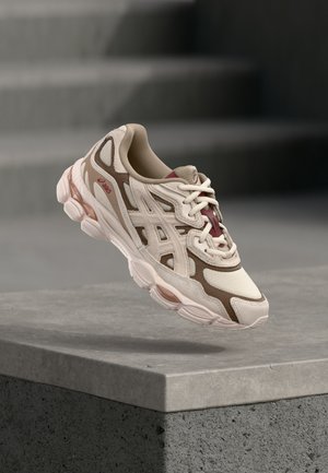 Scarpe da corsa beige e marroni con tomaia in mesh e sintetico, caratterizzate da una suola testurizzata, un design aerodinamico e dettagli rosa.