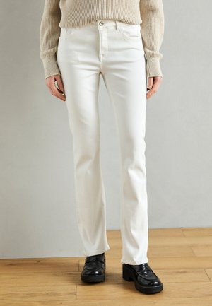 Biele rifle s priliehavým strihom, z bavlny, so zapínaním na gombíky a prednými vreckami, v kombinácii s čiernymi hrubými topánkami.