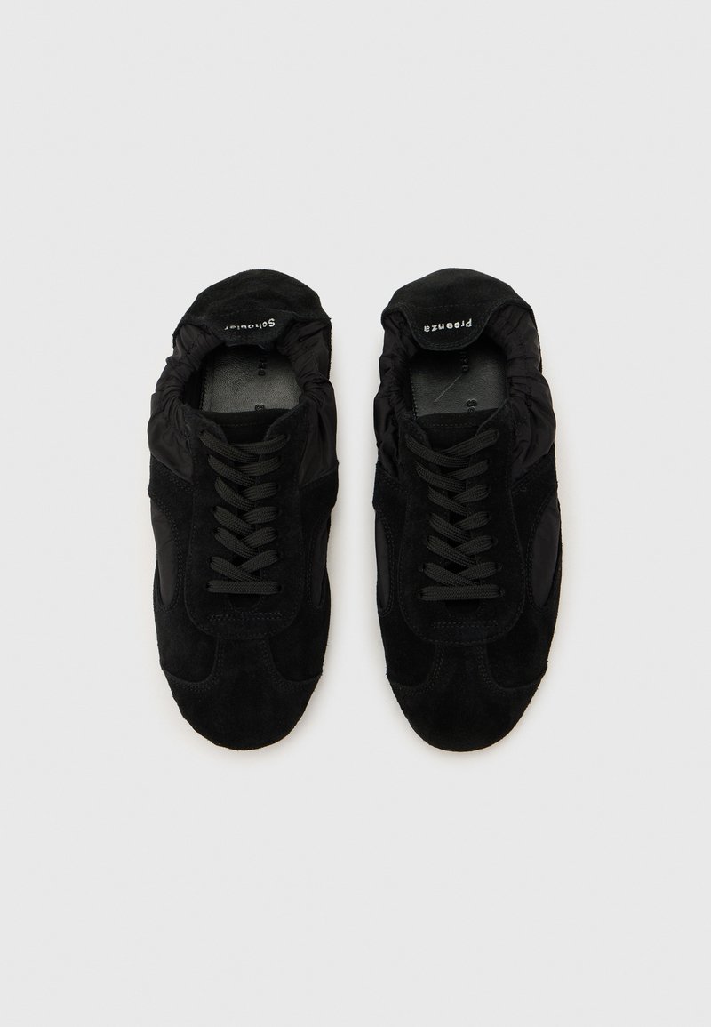 Paire de baskets noires à lacets avec panneaux en daim et tissu, vue de dessus sur un fond clair uni.