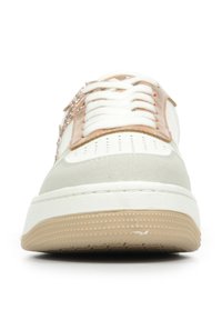 Baskets blanches et beiges avec une semelle texturée, un col rembourré et un système de laçage. Présente un détail métallique sur la tige.