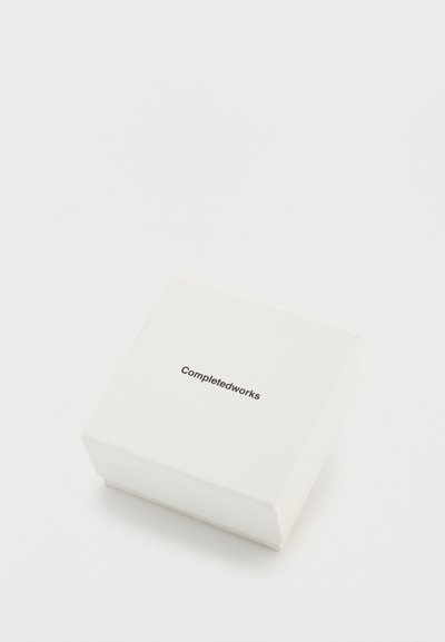 Caixa quadrada branca com acabamento suave, apresentando o texto "Completedworks" em fonte preta simples no topo.