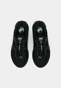 Μαύρα αθλητικά παπούτσια Nike Vomero 5 με επάνω μέρος από δίχτυ, εμφανές σύστημα κορδονιών, υφή στη σόλα και κυκλικό λογότυπο στις εσωτερικές σόλες.