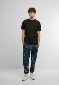 Sort bomulds t-shirt parret med sorte bukser med et blåt abstrakt mønster, elastiske manchetter og hvide sneakers. Simpelt design.