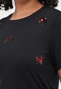 Svart kortärmad t-shirt med broderade röda rosor och gröna detaljer, rund halsringning och mjuk tygtextur.