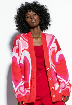 Czerwono-różowy sweter z dzianiny z wzorem w serca, z głębokim dekoltem w kształcie V, z zapięciem na guziki i prążkowanymi mankietami.