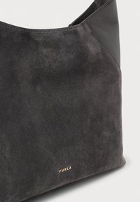 Geantă din piele întoarsă și piele închisă la culoare, cu logo-ul "Furla" auriu pe partea din față jos, prezentată pe un fundal deschis, simplu.