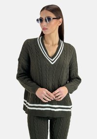 Maglione a maglia verde oliva con motivi a trecce, scollo a V, dettagli a strisce bianche sul colletto e sull'orlo, maniche lunghe, abbinato a pantaloni coordinati.