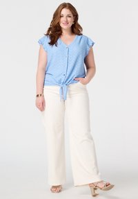 Blouse bleu clair à manches courtes, à boutonnière, avec des détails en oeillet et un devant noué, associée à un pantalon large blanc et des sandales à talons dorés.