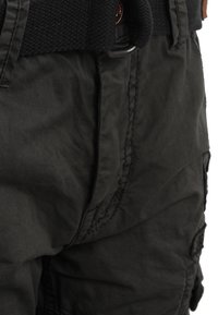 Svarta cargobyxor med en strukturerad finish, med ett brett, vävt bälte och synlig sömnad. Sidfickor finns på benen.