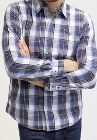 Paidat, joissa on ruudullinen kuvio sinisessä, violetissa ja valkoisessa. Ominaisuuksiin kuuluvat pitkät hihat, rintatasku ja kevyt kangas pehmeällä tekstuurilla.