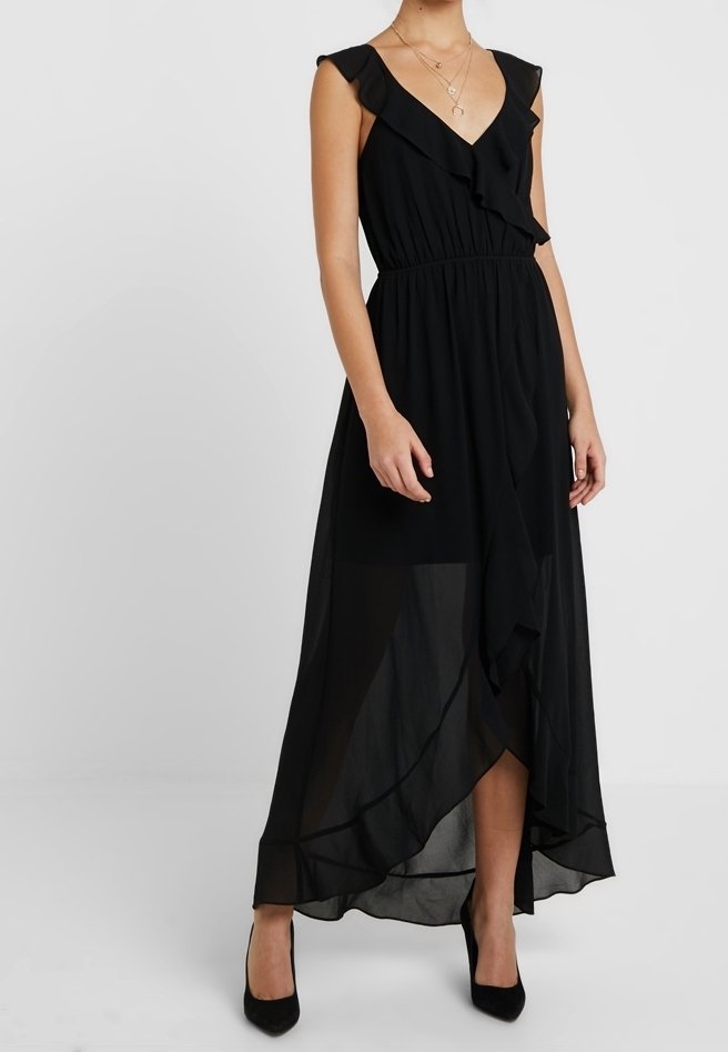 Robe maxi noire avec encolure en V à volants, taille élastique et ourlet asymétrique. Fabriquée en tissu léger et transparent, portée avec des talons.