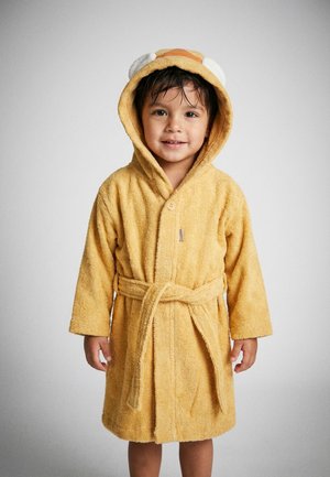 Junges Kind trägt einen weichen gelben Kapuzenbademantel mit Bärenohren, lächelt und steht vor einem schlichten hellen Hintergrund.