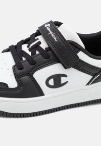 Baskets en noir et blanc avec des matériaux en cuir et synthétiques, des accents texturés, un système de fermeture à lacets et une bande Velcro, avec un logo.