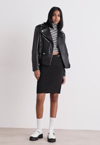 Crna kožna motoristička jakna preko prugaste rolke, uparena s crnom olovkom suknjom, bijelim čarapama i čvrstim bijelim cipelama.