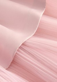 Gaiši rozā audums, kas izgatavots no gluda satīna un caurspīdīgiem, teksturētiem tilla slāņiem, radot mīkstu, slāņotu izskatu.