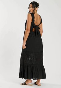 Svart maxiklänning med volangkrage, öppen rygg och knytdetalj. Har intrikata utskärningar och en fladdrig nederkant.