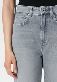 Visoko pasovane, svetlo sivo denim jeans hlače z gladko teksturo, petimi žepi in srebrnimi dodatki. Imajo gumb in zadrgo za zapiranje.