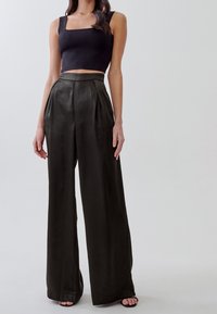 Top cropped nero abbinato a pantaloni a vita alta, larghi e verde scuro con pieghe e una consistenza liscia, indossati con scarpe aperte.