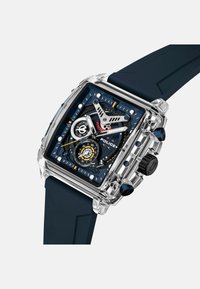 Montre carrée avec boîtier transparent, bracelet en silicone navy, cadran bleu comportant trois sous-cadrans, design d'engrenage complexe et accents métalliques.