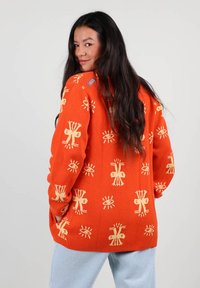Pull en laine orange avec des motifs abstraits jaunes, à coupe décontractée et col rond, présenté sur un fond neutre.