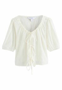 Blouse blanche texturée avec un décolleté en V profond, un devant noué et des manches courtes bouffantes. Présente des rayures verticales subtiles.